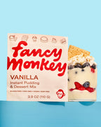 Fancy Monkey Vanilla Instant Pudding & Dessert Mix pouch beside a layered berry dessert on a blue background